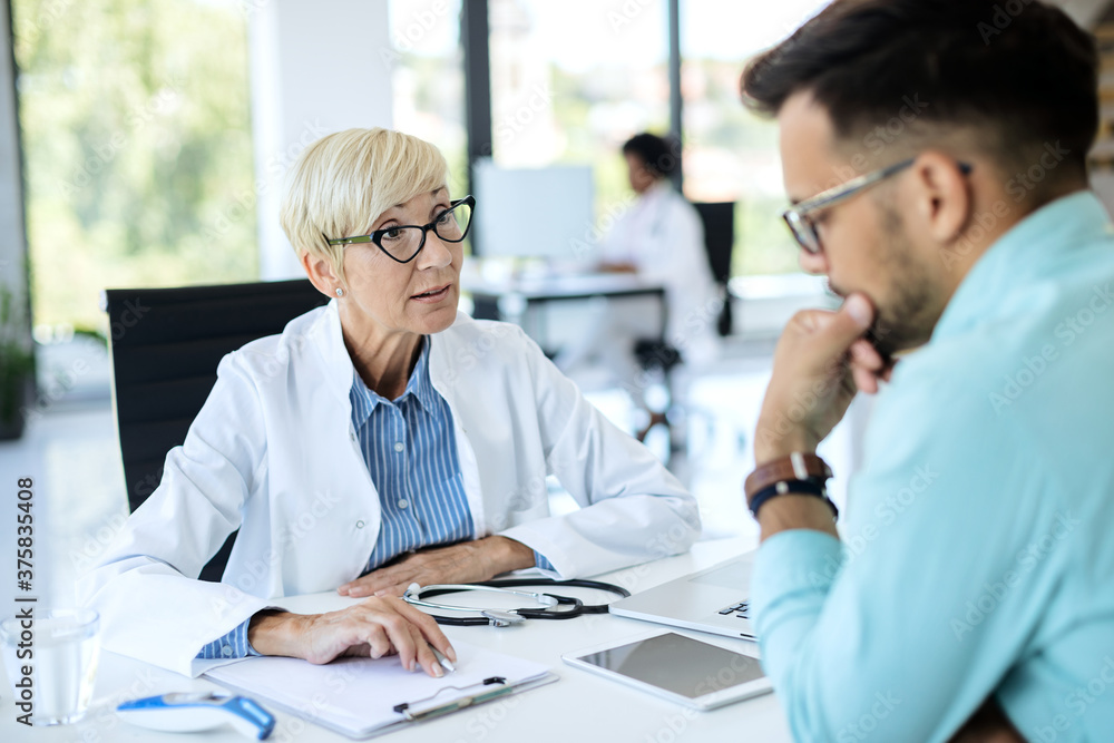 Mature doctor communicating with her patient while analyzing his medical data at the clinic. Mature doctor communicating with her patient while analyzing his medical data at the clinic.