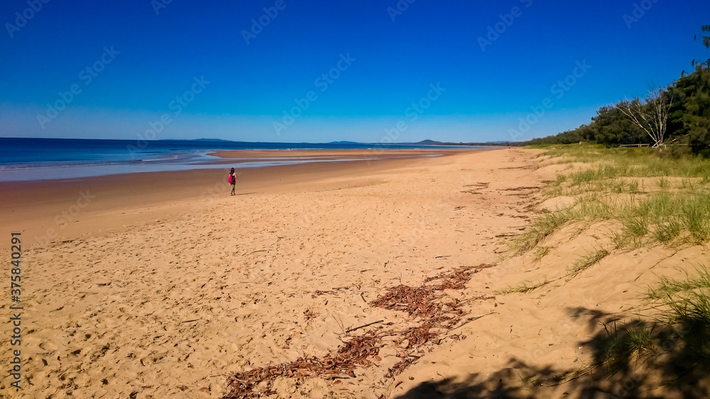 A woman, walking all alone on an infinite beach in queensland australia