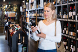 Middle aged woman looking for perfect wine for solemn occasion in wine store