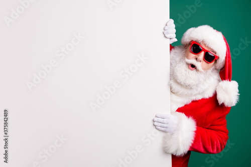 Photo of retired stylish grandpa grey hair hold white empty board offer newyear weekend novelty wear red santa x-mas costume coat gloves sunglass cap isolated green color background photo