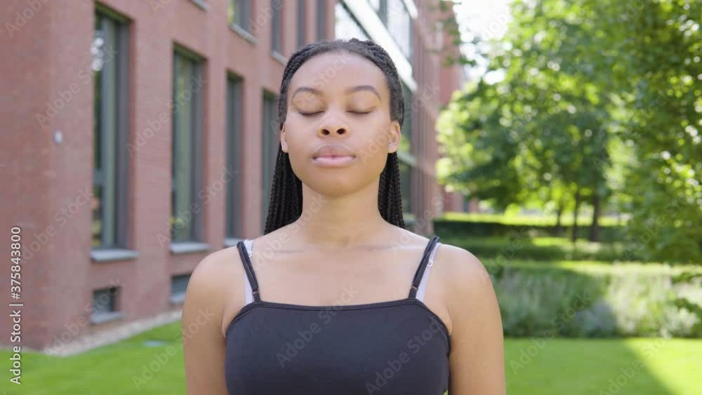 A young black woman looks seriously at the camera - an office building and green park in the background A young black woman looks seriously at the camera - an office building and green park in the background