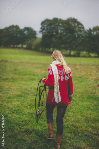 Woman with horse harness in hand walking on meadow photo