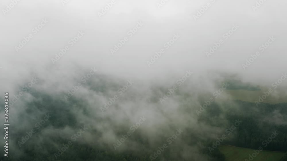 Aerial top view drone flies through heavenly fluffy rain clouds rolling over green forest and field. Foggy morning in pine woodland from above, cloudy, misty weather. Camera flight in low cloud in sky Aerial top view drone flies through heavenly fluffy rain clouds rolling over green forest and field. Foggy morning in pine woodland from above, cloudy, misty weather. Camera flight in low cloud in sky
