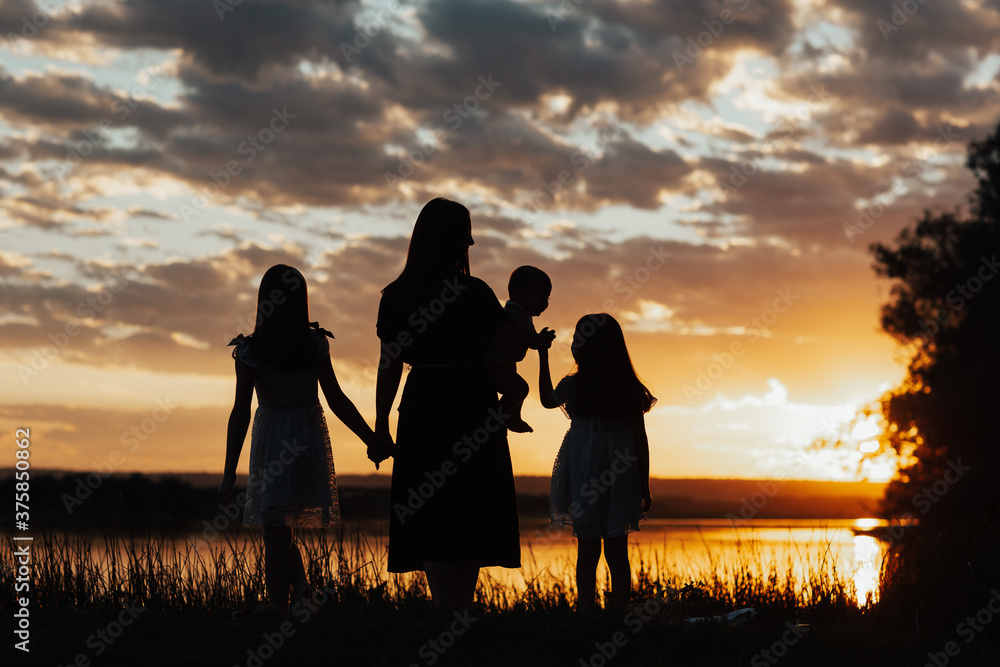 Family having a walk at sunset, the infant boy sitting on his mother's hand and two daughter standing near. Tranquil and peaceful time together.