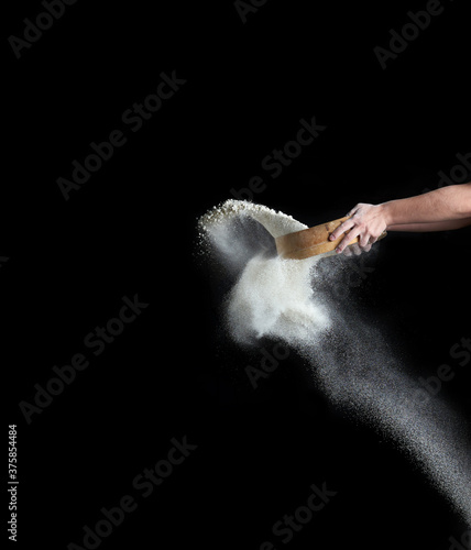 female hand sifts white wheat flour through a round wooden sieve on a black background
