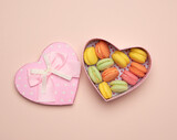 round baked multicolored macarons lie in a pink cardboard box in the shape of a heart