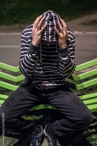 problematic, the hooded man on a bench holding his head