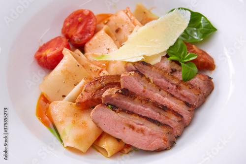 Close up view on cooked pasta and sliced duck breast with sauce and parmesan with copy space. Shallow dof.