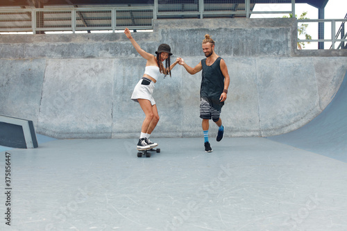Couple At Skatepark. Happy Guy And Girl In Casual Outfit Riding On Skateboard. Extreme Sport And Skateboarding As Urban Subculture. Lifestyle Of Active People In City.