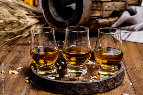 Small tasting glasses with aged Scotch whisky on old dark wooden vintage table with barley grains