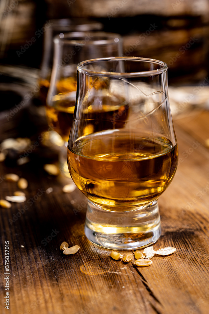 Small tasting glasses with aged Scotch whisky on old dark wooden vintage table with barley grains Small tasting glasses with aged Scotch whisky on old dark wooden vintage table with barley grains