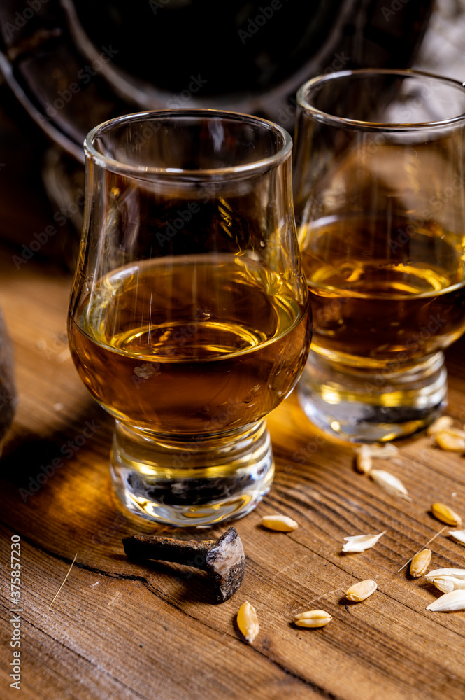Small tasting glasses with aged Scotch whisky on old dark wooden vintage table with barley grains Small tasting glasses with aged Scotch whisky on old dark wooden vintage table with barley grains
