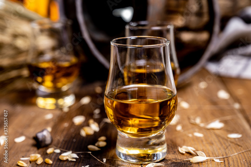 Fototapeta Naklejka Na Ścianę i Meble -  Small tasting glasses with aged Scotch whisky on old dark wooden vintage table with barley grains