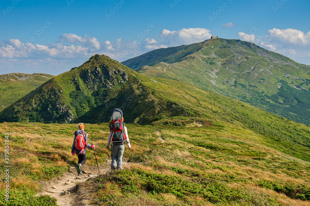 Mom and daughter with backpacks are walking along a mountain trail in the Carpathian Mountains. Ukraine