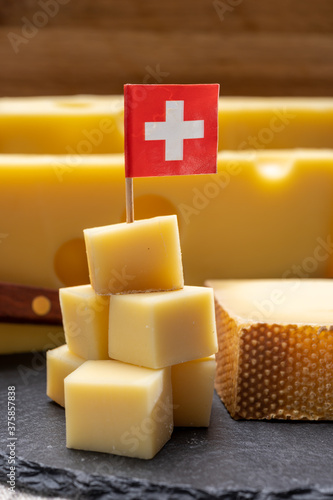 Swiss cheeses, block of medium-hard yellow cheese emmental or emmentaler with round holes and matured gruyere served in cubes as mountain top with Swiss flag.