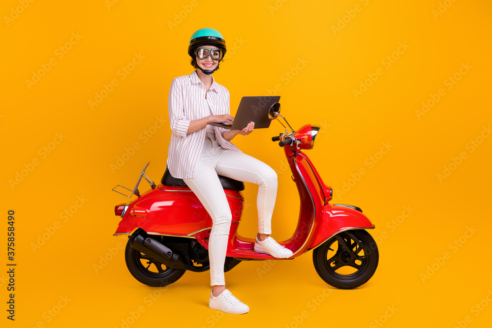 Full body photo of positive biker girl sit motor bike use laptop search browse map online navigation wear helmet goggles striped shirt pants trousers isolated bright shine color background Full body photo of positive biker girl sit motor bike use laptop search browse map online navigation wear helmet goggles striped shirt pants trousers isolated bright shine color background