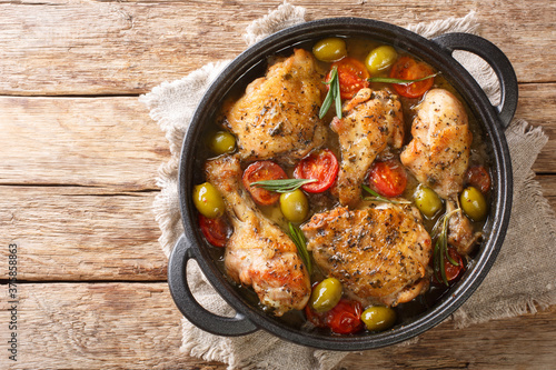 Delicious chopped chicken baked with green olives, tomatoes and onions, herbs close-up in a frying pan on the table. horizontal top view from above photo