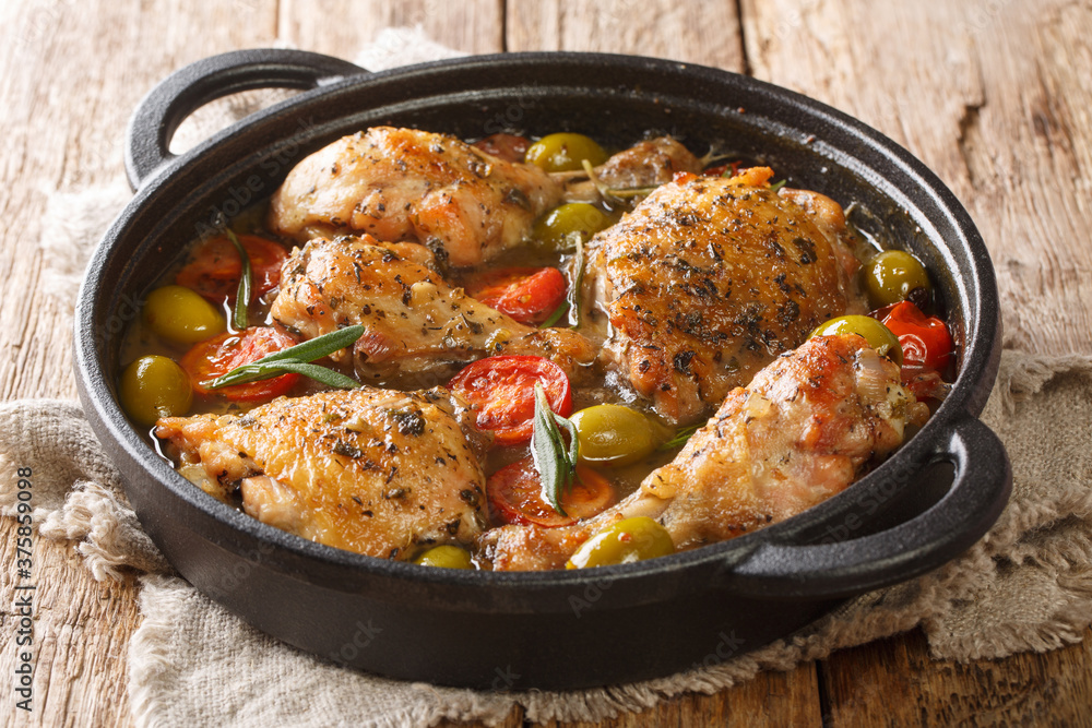 Fototapeta premium Homemade French chicken baked with green olives, tomatoes and onions, herbs close-up in a frying pan on the table. horizontal