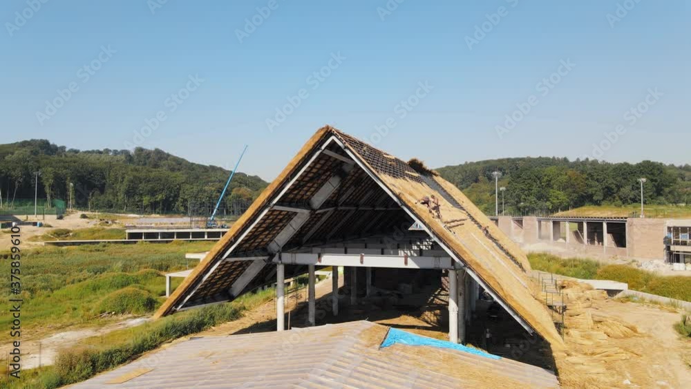 Aerial view the roof of a large house with dry straw and hay. Workers who install the roof. Aerial view the roof of a large house with dry straw and hay. Workers who install the roof.