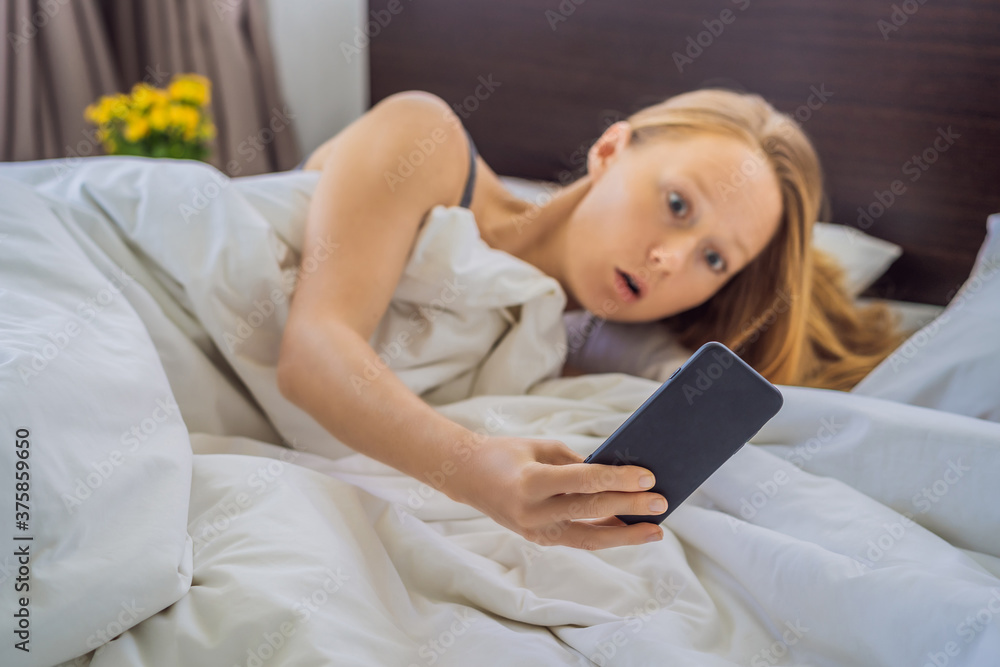 Overslept woman with surprised expression while looking at phone after missed the alarm and woke up late Overslept woman with surprised expression while looking at phone after missed the alarm and woke up late