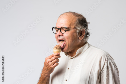 retired Indian old man eating ice cream, standing icolated against white background photo