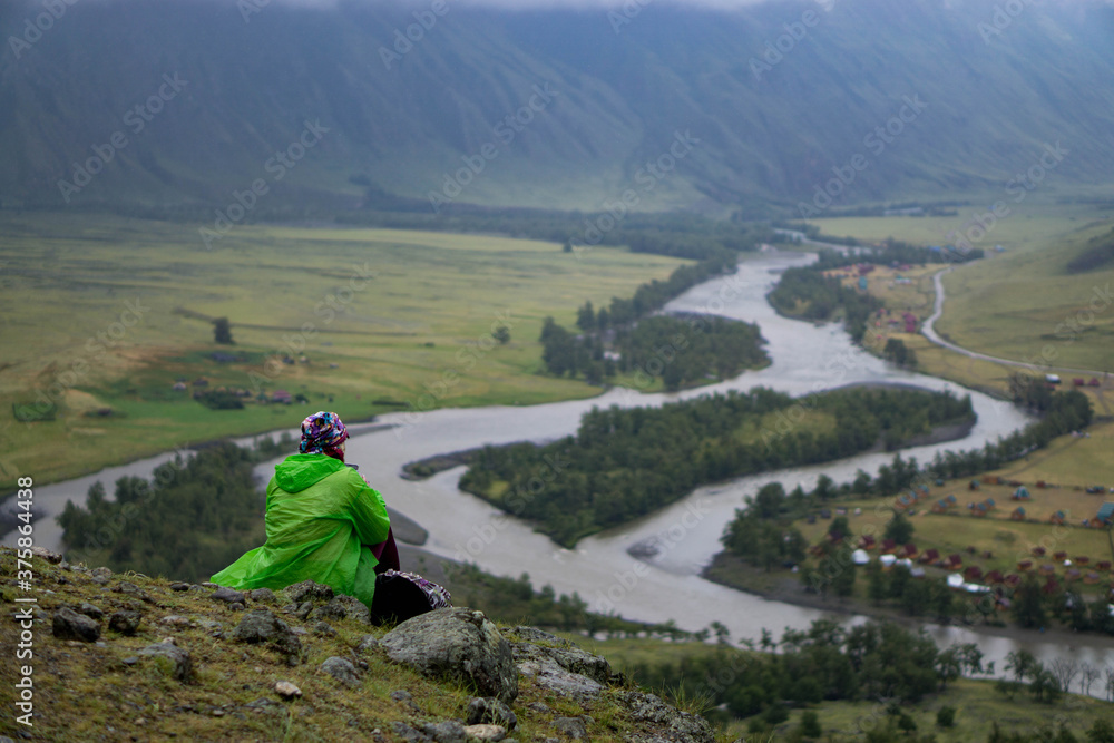 A woman sitting on top with a view of the valley of a mountain river. Russia, Altai Republic, Ulagansky District, Chulyshman River, Akkrum tract