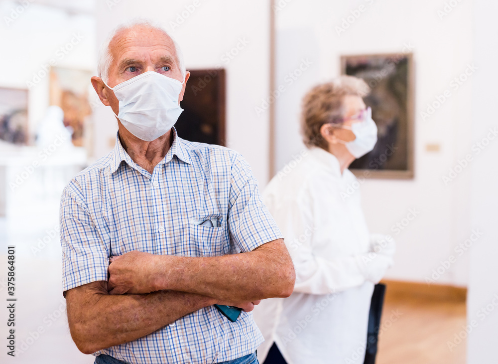 Obraz premium mature man in mask protecting against covid examines paintings on display in hall of art museum