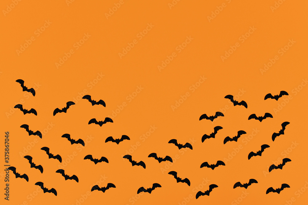 Halloween deco confetti in shape of small flying black bats on orange background with empty copy space