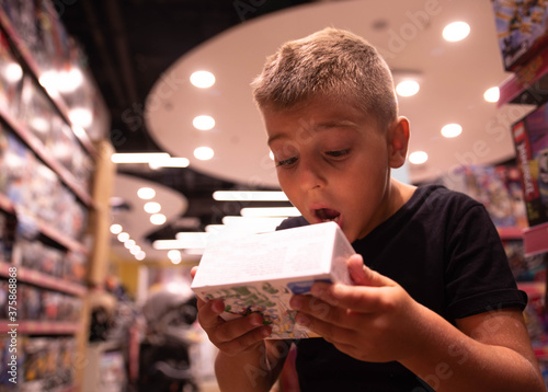 A happy little boy in a toy store looks enthusiastically at the box