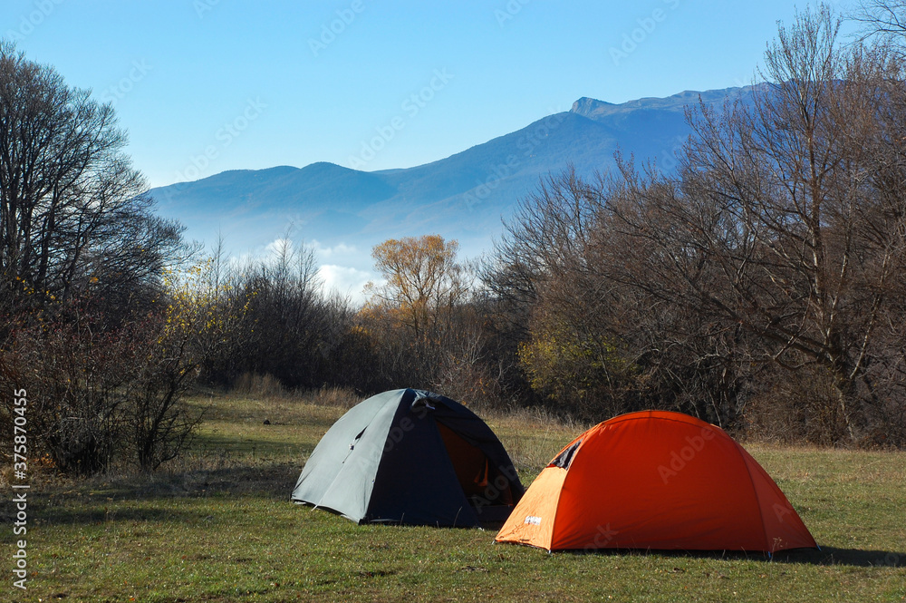 Two tents in a meadow against the backdrop of a mountain in the autumn