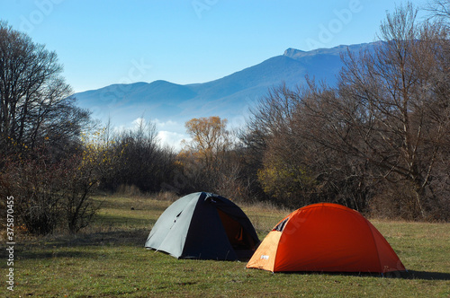 Two tents in a meadow against the backdrop of a mountain in the autumn