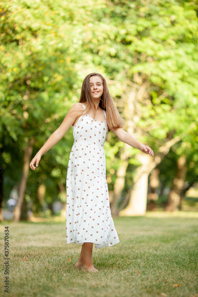 beautiful girl in a light white dress with polka dots is spinning in the park on the grass beautiful girl in a light white dress with polka dots is spinning in the park on the grass
