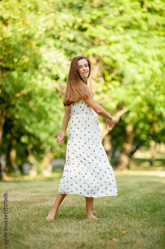 beautiful girl in a light white dress with polka dots is spinning in the park on the grass