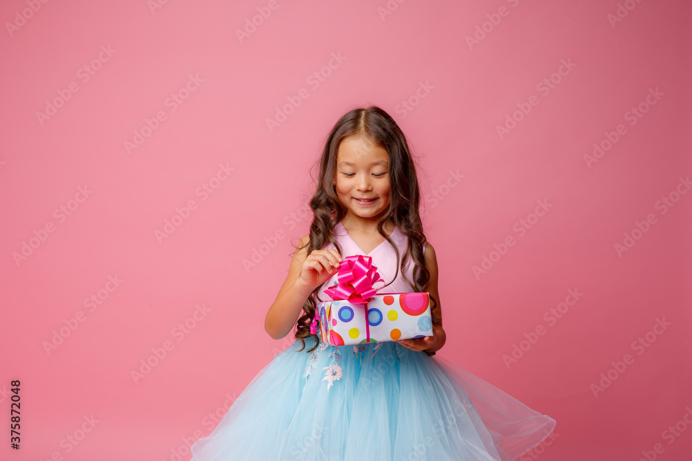 a little girl of Asian appearance holds a gift in her hands celebrating her birthday on a pink background