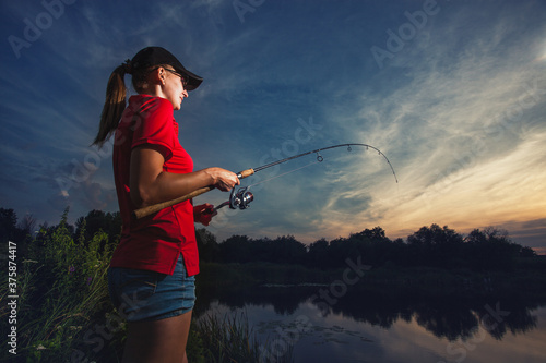 Cute woman is fishing with rod on lake Fototapet