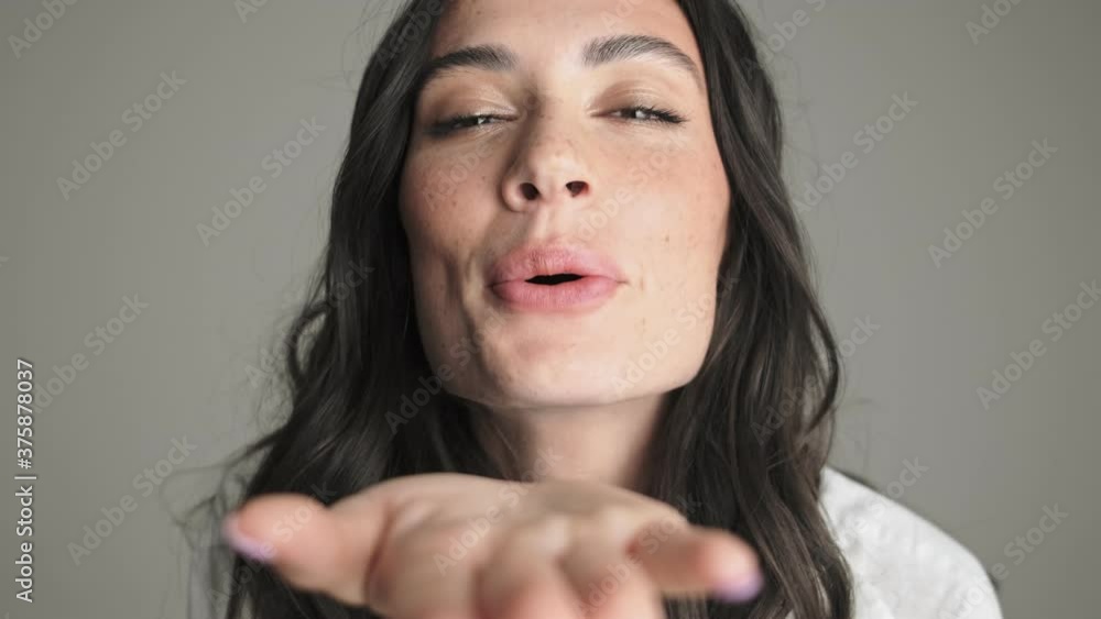 A beautiful young woman is sending an air kiss to the camera standing isolated over gray background A beautiful young woman is sending an air kiss to the camera standing isolated over gray background