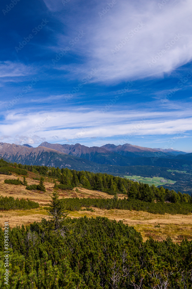 View over the gentle mountain slopes of the Moserkopf (high moor) in Lungau in Austria. In the foreground pine forests. Picturesque cloud figures in the sky.