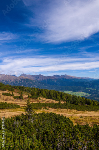 View over the gentle mountain slopes of the Moserkopf (high moor) in Lungau in Austria. In the foreground pine forests. Picturesque cloud figures in the sky.