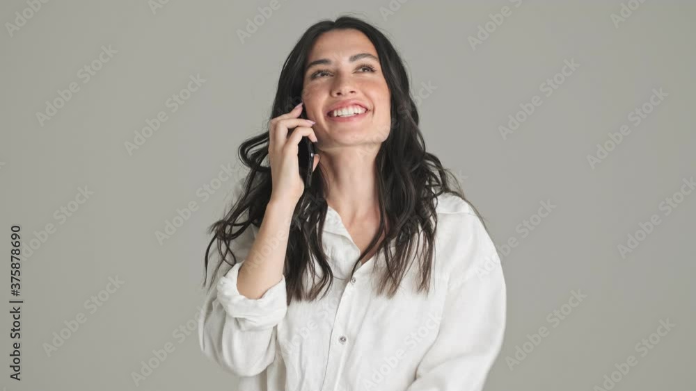 A smiling young woman is talking on the phone and jumping standing isolated over gray background A smiling young woman is talking on the phone and jumping standing isolated over gray background