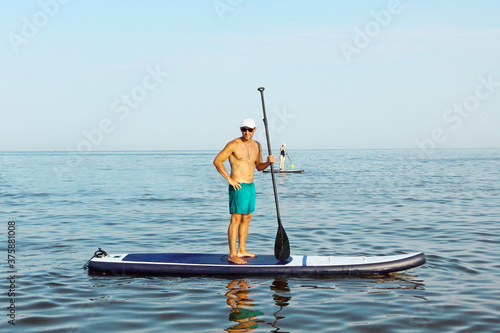 Man is training on a SUP board in the blue sea.