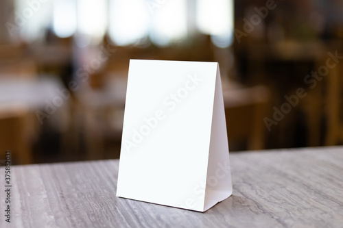 Mock up Label the blank menu frame in Bar restaurant. Stand for booklet with white sheet paper acrylic tent card on table wiht blurred background can inserting the text or picture