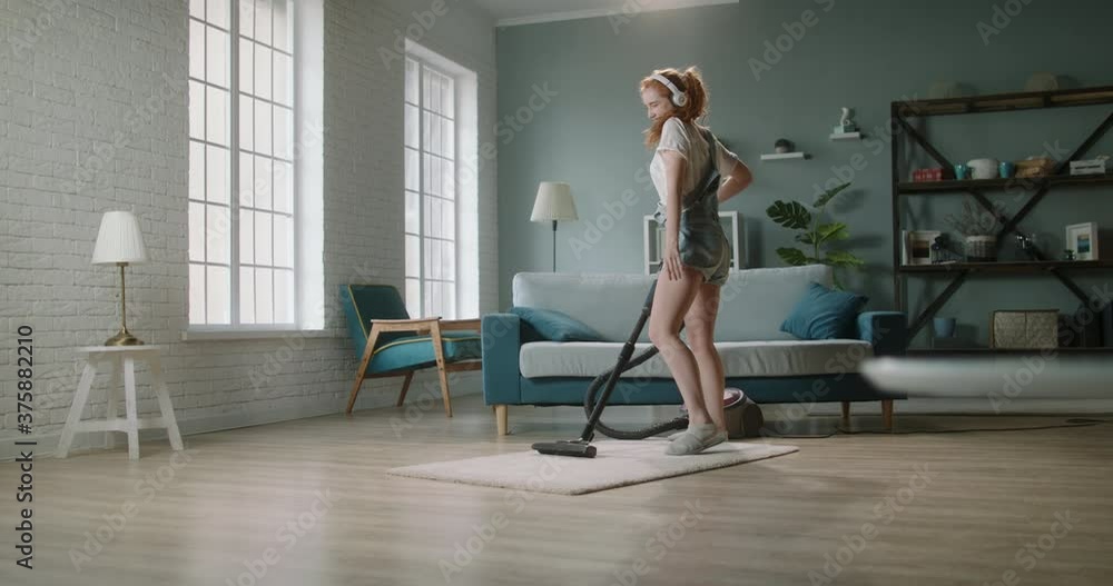 Young positive caucasian woman funnily dancing while cleaning the house. Cute girl enjoys tidying her home, using vacuum cleaner and listening to music - happy people 4k footage Young positive caucasian woman funnily dancing while cleaning the house. Cute girl enjoys tidying her home, using vacuum cleaner and listening to music - happy people 4k footage