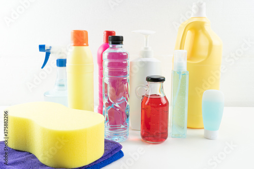 Plastic bottles of cleaning products set with pile clothes on table background.