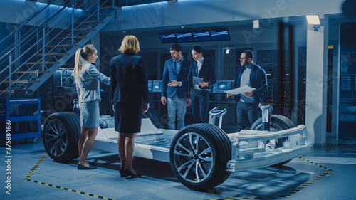 Diverse Team of Automobile Design Engineers Introducing Futuristic Autonomous Electric Car Platform Chassis to a Group of Investors and Businesspeople. Vehicle Frame with Wheels, Engine and Battery © Gorodenkoff