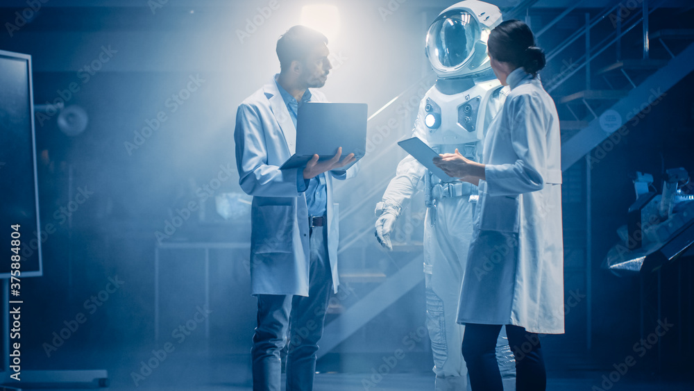 Diverse Team of Aerospace Scientists and Engineers Wearing White Coats have Discussion, Use Computers, Design New Space Suit Adapted for Galaxy Exploration and Travel. Constructing Astronaut Suit Diverse Team of Aerospace Scientists and Engineers Wearing White Coats have Discussion, Use Computers, Design New Space Suit Adapted for Galaxy Exploration and Travel. Constructing Astronaut Suit