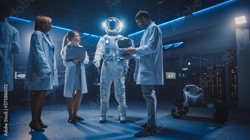 Team of Aerospace Scientists and Engineers Wearing White Coats have Discussion, Use Computers, Construct Astronaut Helmet for New Space Suit Adapted for Exploration and Travel. Low Angle Shot