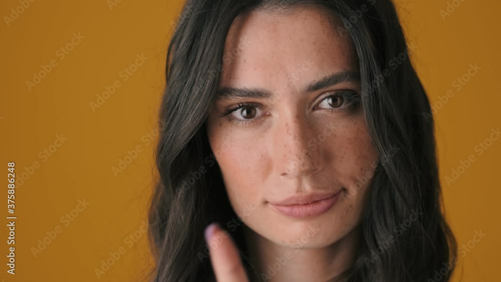 A close-up view of a displeased angry young woman is showing secret gesture standing isolated over yellow background A close-up view of a displeased angry young woman is showing secret gesture standing isolated over yellow background