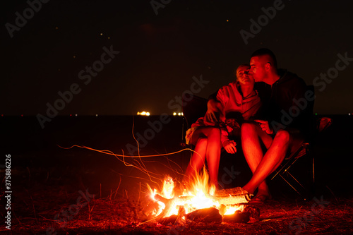 Happy Young couple sitting by the fire. Big bonfire and young couple in the background. Long exposure photo.