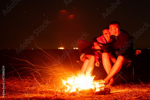 Happy Young couple sitting by the fire. Big bonfire and young couple in the background. Long exposure photo.