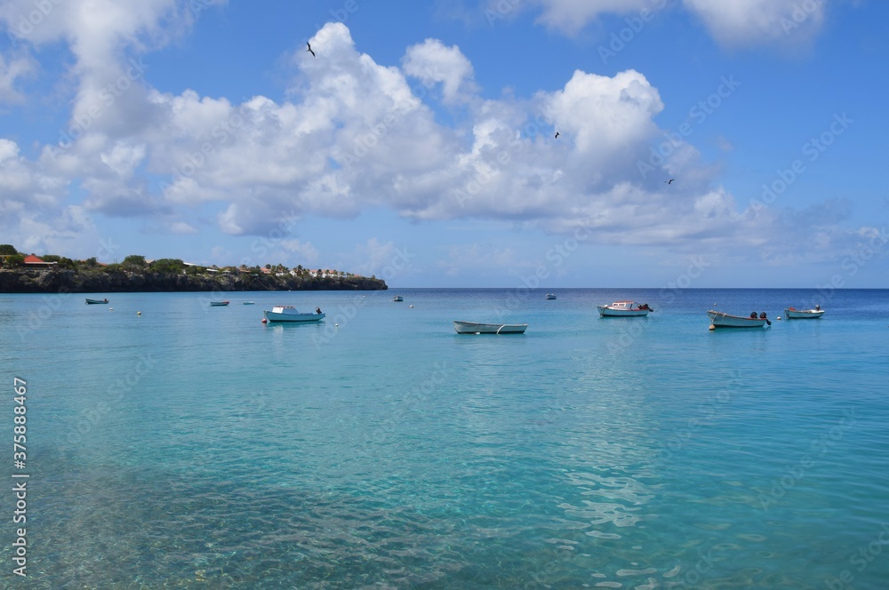 Cloudy sky and fishing boats in the turquoise water at Playa Grandi at Westpunt Curacao
